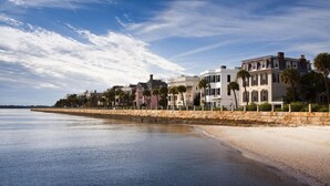 A beachfront hotel with a stone wall, palm trees, and a clear sky.