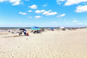 Uma praia com pessoas relaxando sob guarda-sóis, cadeiras de praia e uma rede de voleibol.
