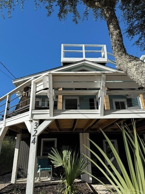 Un bâtiment à deux étages doté d’un balcon, d’un numéro de maison bien visible et d’un arbre au premier plan.