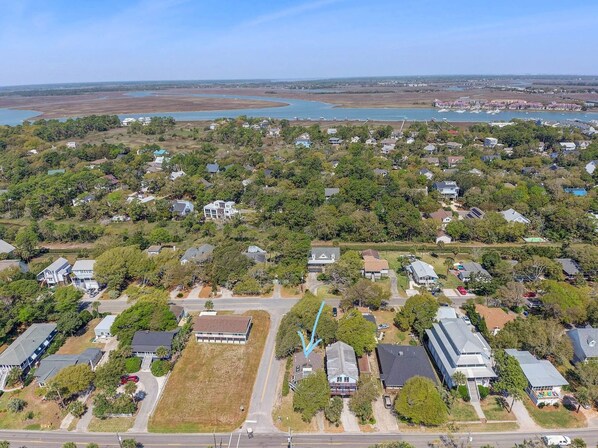 An aerial view of a residential area with houses, a large open grassy field, and a body of water in the background.