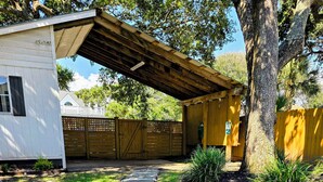 Un chemin mène à un patio abrité doté d’une terrasse en bois et d’un petit bâtiment.
