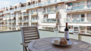 A table with a plate of food, a bottle of wine, and two wine glasses on a balcony overlooking a residential area.