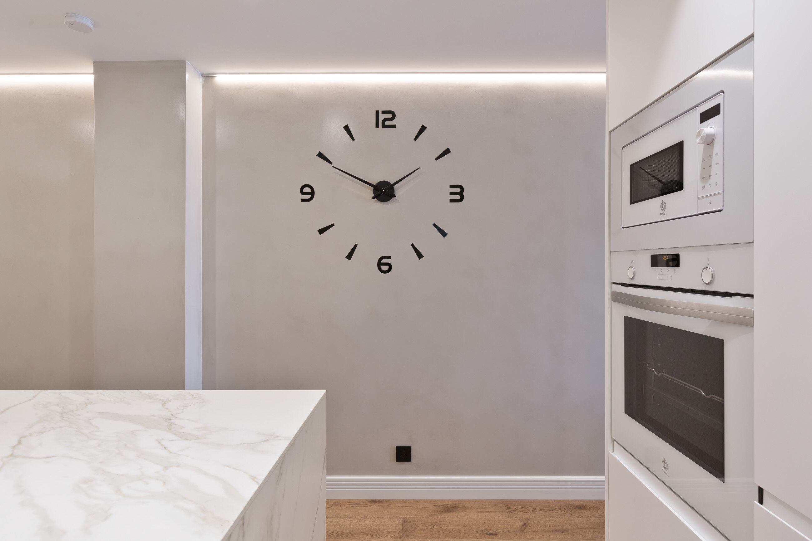 A kitchen with a built-in clock, a microwave, and a stove.