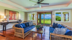 A spacious living room with wicker furniture, a ceiling fan, and a view of the ocean through large sliding doors.