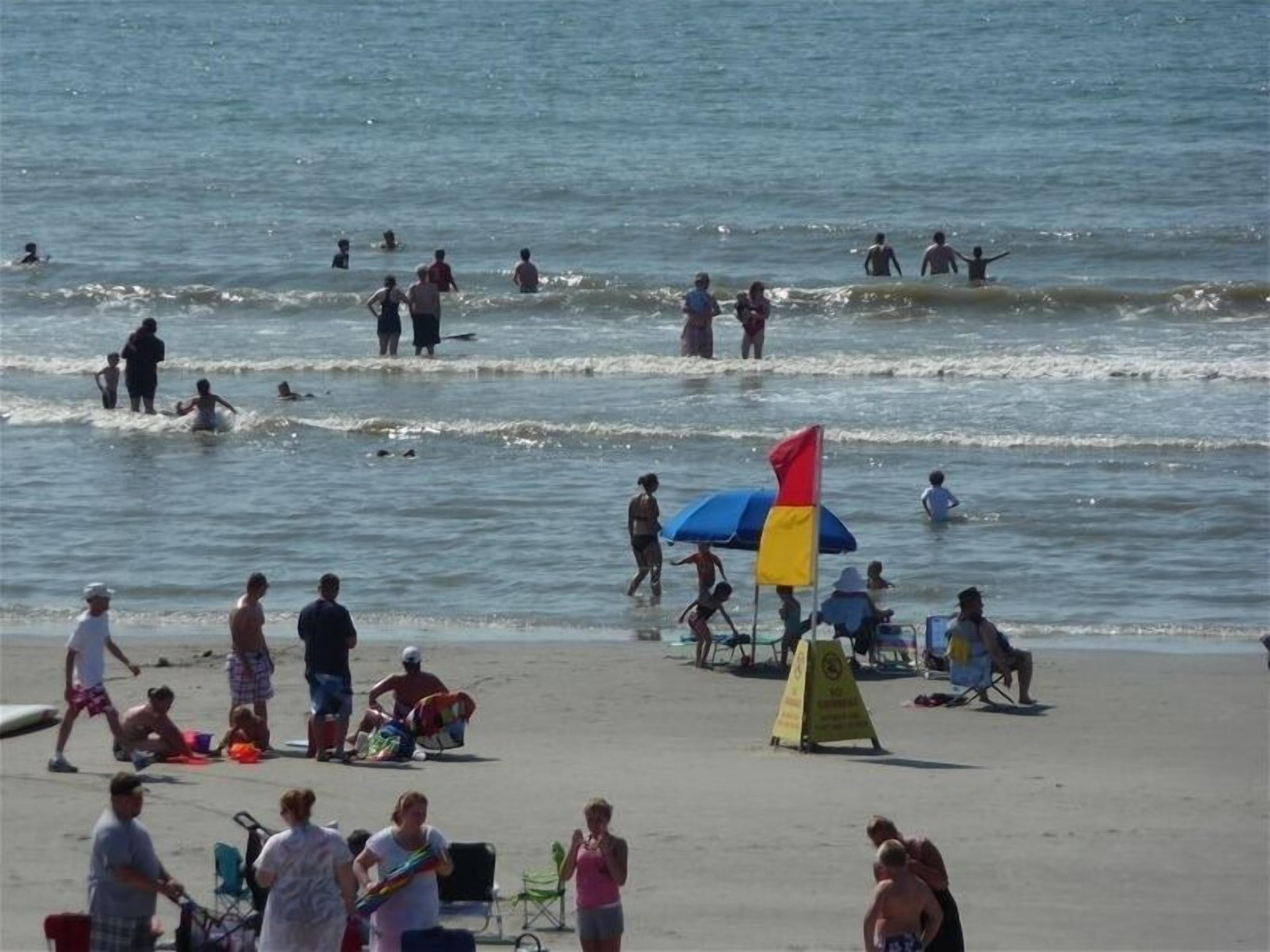 A beach with people swimming and sunbathing. There are beach chairs and umbrellas.
