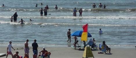 A beach with people swimming and sunbathing. There are beach chairs and umbrellas.