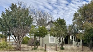 A house with a fenced yard, surrounded by trees and a clear sky.