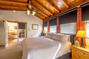 A bedroom with a large bed, wooden ceiling beams, a ceiling fan, and a window with curtains. - Large 4 bed, 2 bath luxury home, views, patios for up to 8 guests (Bisbee)