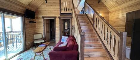 A wooden interior with a staircase, a red sofa, and a patterned carpet.