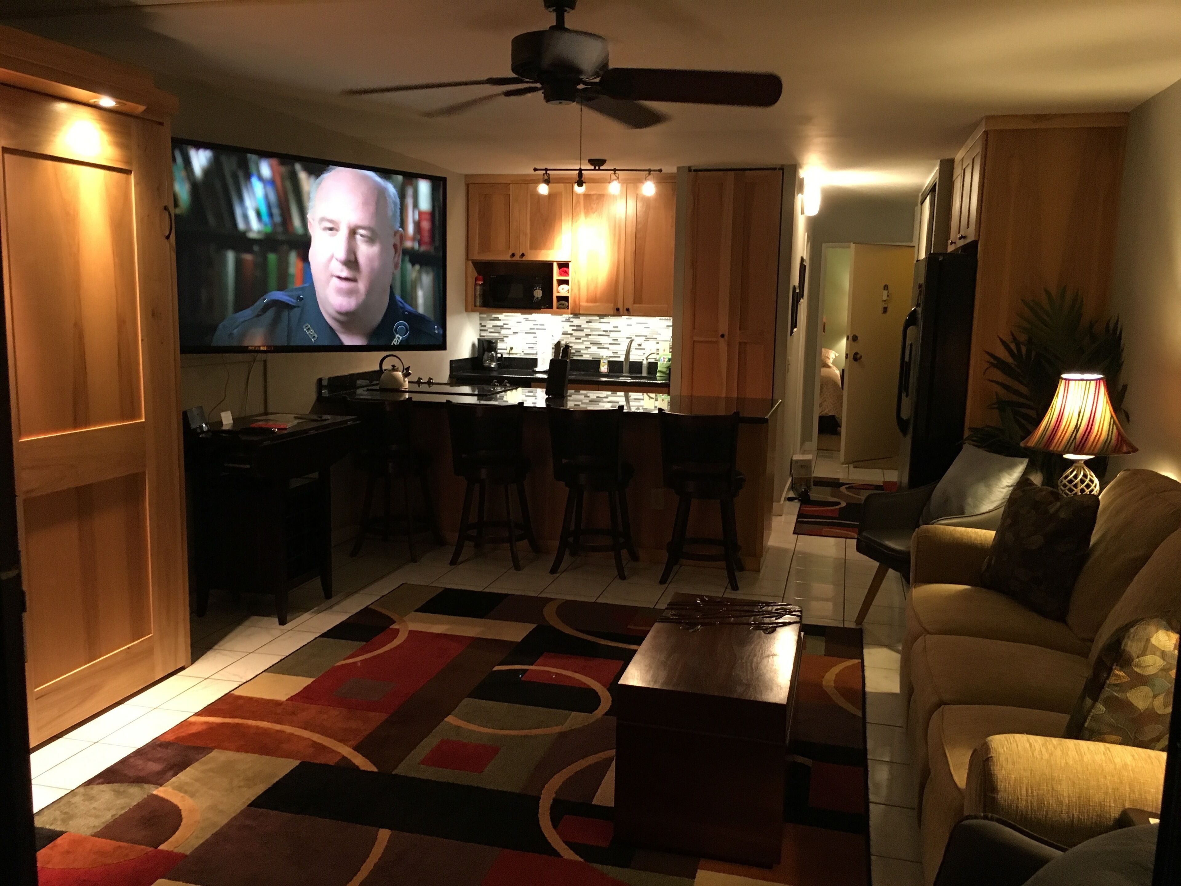 A living room with a television, a sofa, a coffee table, and a kitchen area with wooden cabinets and a bar.