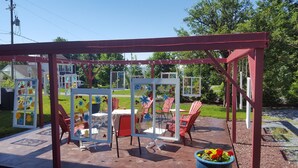 Ein überdachter Patio-Bereich mit rotem Rahmen, Glasverkleidung und Gartenmöbeln.