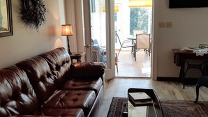 Ein Wohnzimmer mit einer Ledersofa, einem Tisch mit Lampe und Blick auf die Terrassenanlage.