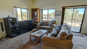 A living room with a large flat-screen TV, two sofas, a coffee table, and a bookshelf. - Endless Tucson Desert Views 3Br2Ba Home 2 Acres Garage Arcade Games Nature Oasis (Tucson)