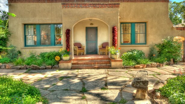 A building with a brick roof, a front porch with two chairs, and a door.