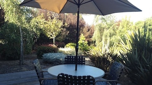 Une terrasse extérieure avec une table ronde et quatre chaises, entourée d’une plateforme en bois et d’une végétation luxuriante.