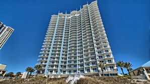Un grand hôtel à plusieurs étages, doté de balcons, situé près d’une plage bordée de palmiers.