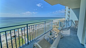 Un balcon avec vue sur la plage et l’océan, aménagé avec une table, des chaises et un canapé.