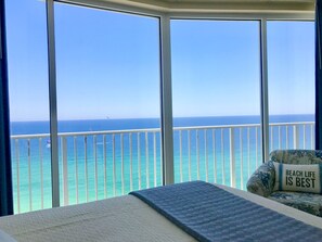 Un balcón con vista al océano, una cama y una silla con un cojín que dice 'BEACH LIFE IS BEST'.