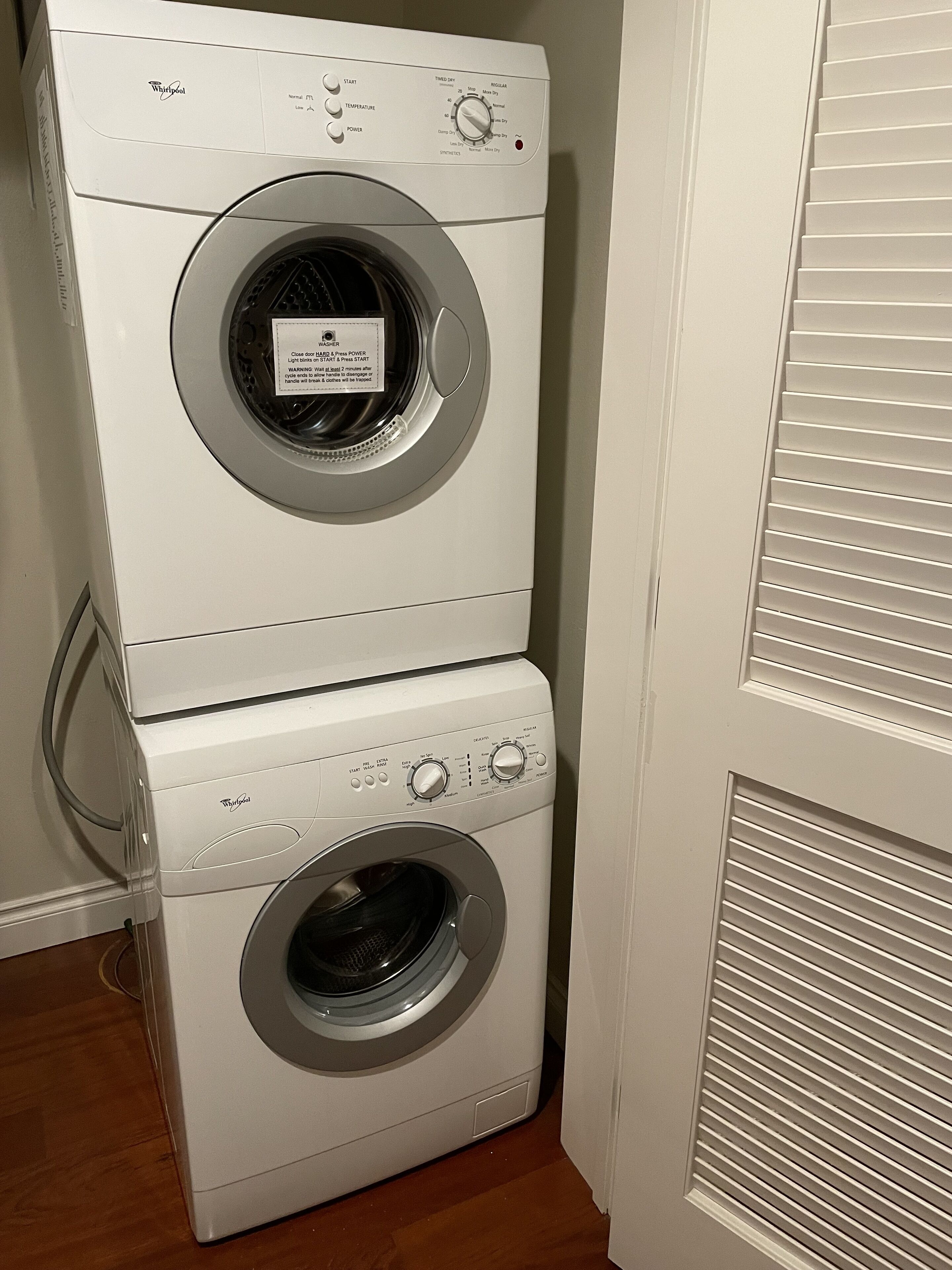 Een gestapelde wasmachine en droger met bedieningsknoppen en een label.