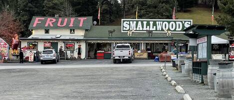 Una pequeña tienda a un lado del camino, llamada 'Fruit' y 'Smallwood's', con un aparcamiento de grava y una fila de barriles.