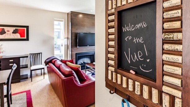 Un salon avec un canapé rouge, un téléviseur et un tableau noir sur lequel on peut lire : « Bienvenue à la Vue ! »