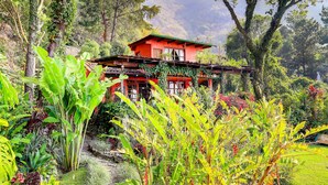 Un bâtiment rouge surmonté d’un toit vert, entouré d’une végétation luxuriante et bordé d’un chemin de pierre.