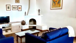 Un salon avec une cheminée, un canapé bleu, une télévision et des tableaux encadrés accrochés au mur.