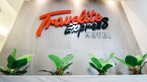 A sign for Travelite Express Hotel with a modern design and green plants at the bottom. - Travelite Express Hotel (Baguio)