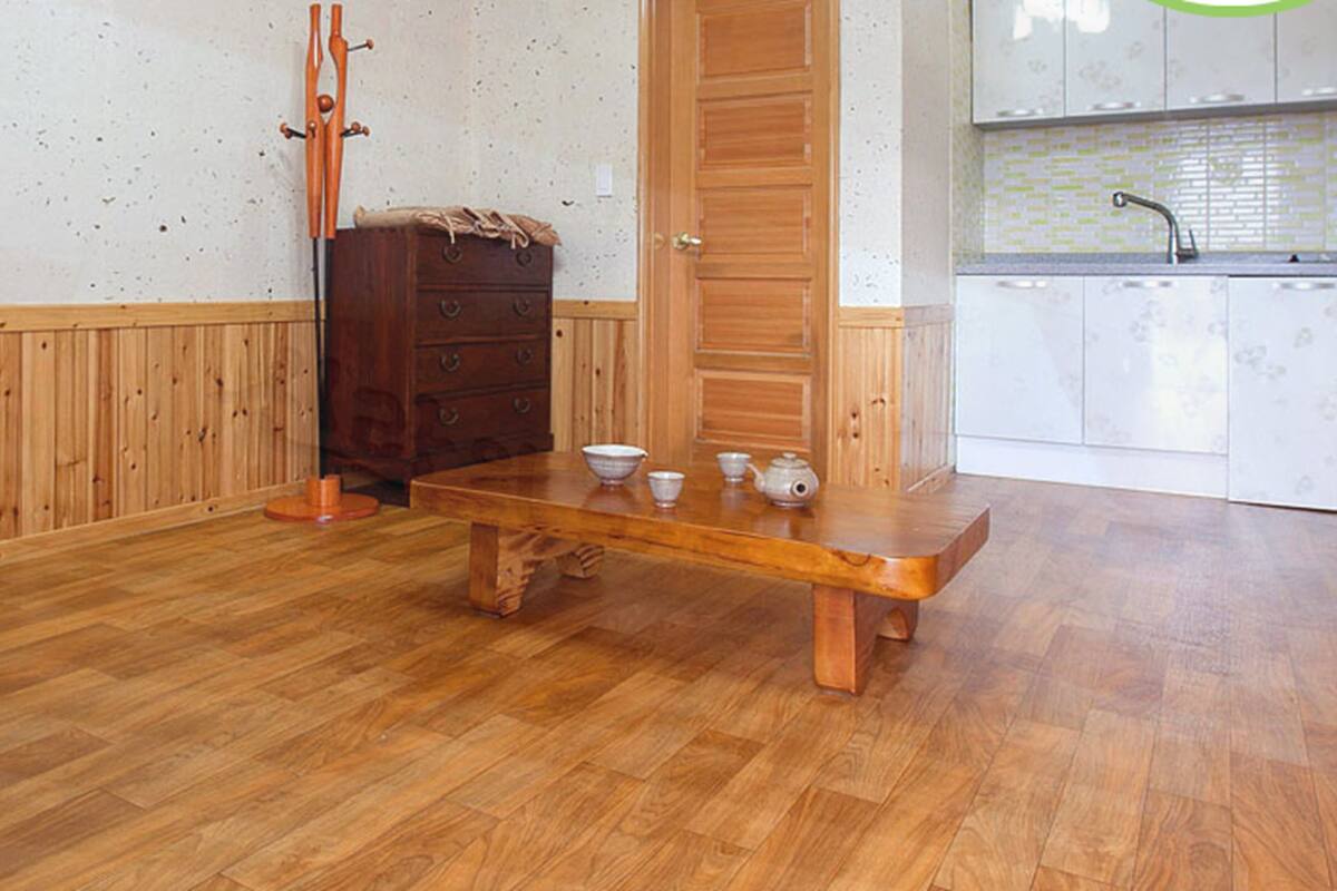 A wooden floor with a dining table set for four, a wooden cabinet, and a kitchen area with a sink and cabinets.
