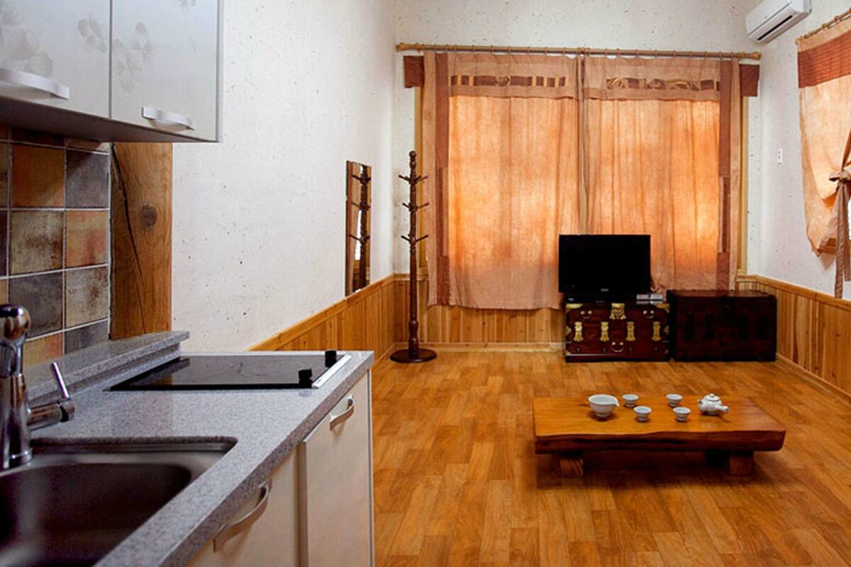 A compact living space with a kitchen area, a dining table with tea sets, and a television.