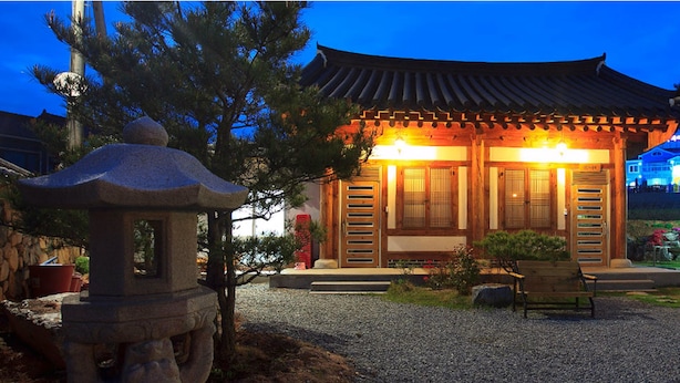 A traditional Korean-style building with a tiled roof, wooden doors, and a stone lantern in the foreground. - Songhak Pension (Gyeongju)