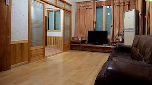 A traditional Japanese-style living room with a wooden floor, a brown leather sofa, a television, and a sliding door leading to another room. - Songhak Pension (Gyeongju)