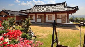 A traditional Korean building with a tiled roof and wooden structure, surrounded by a well-maintained garden with flowering plants. - Songhak Pension (Gyeongju)