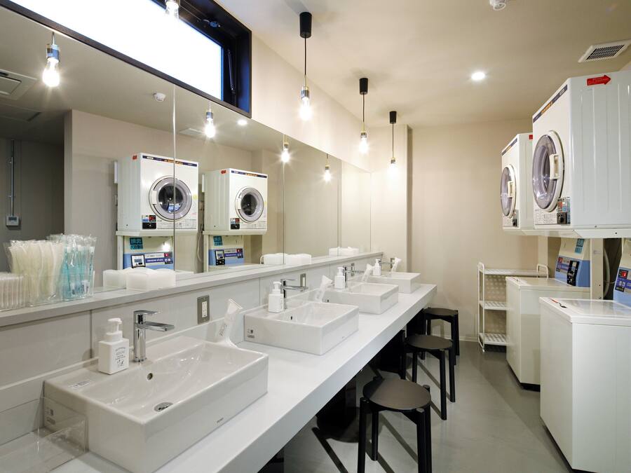 Un baño moderno con varios lavamanos, un espejo grande y varias lavadoras.