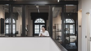 En person som står i en modern interiör med stora fönster och en trappa.