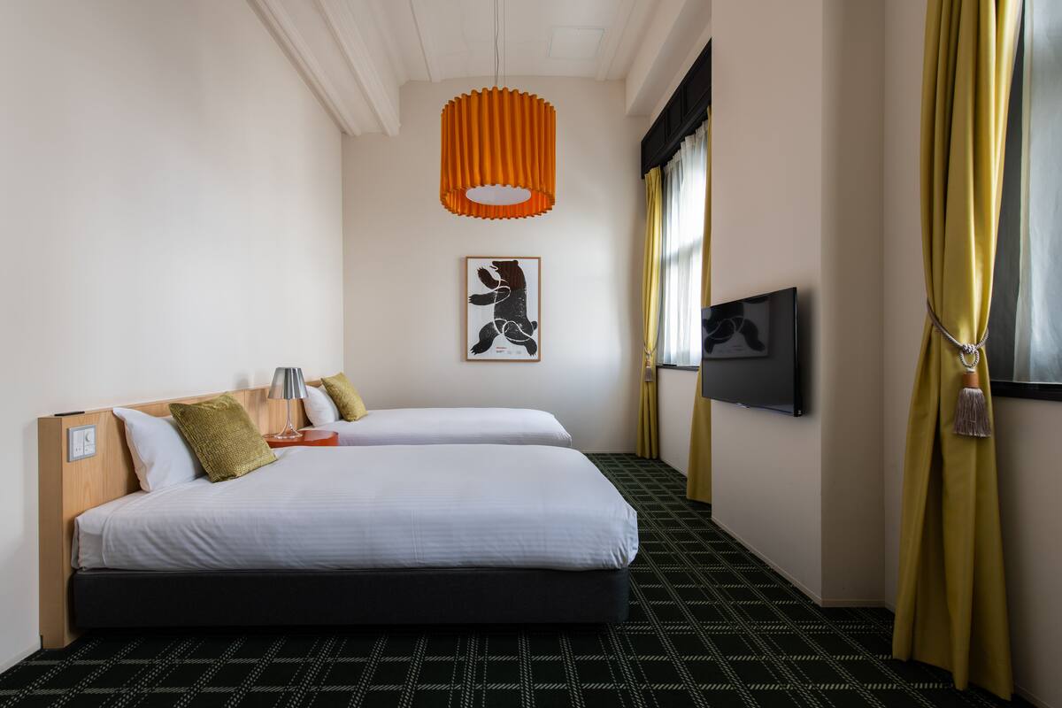 A hotel room with two beds, a mounted TV, a framed artwork, and a unique orange pendant light.