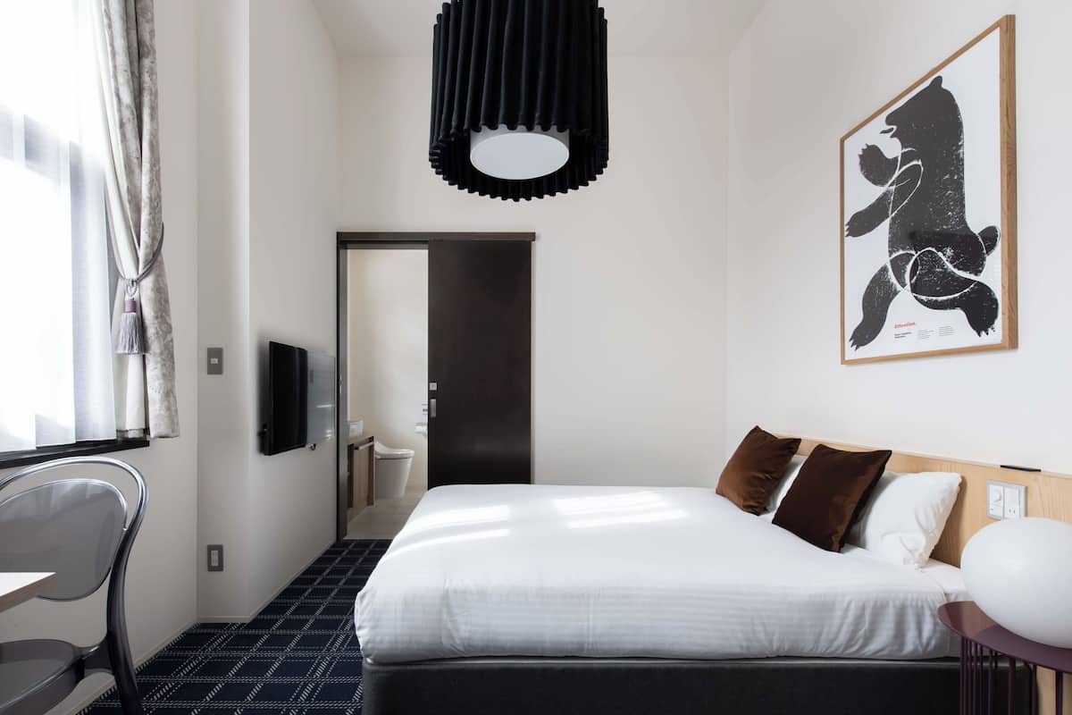 A hotel room with a bed, a desk, a chair, a TV, and a framed artwork on the wall.