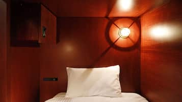 A wooden room with a bed, a wall-mounted light fixture, and a small cabinet.