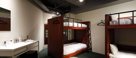 A dormitory room with bunk beds, a desk, and a chair.