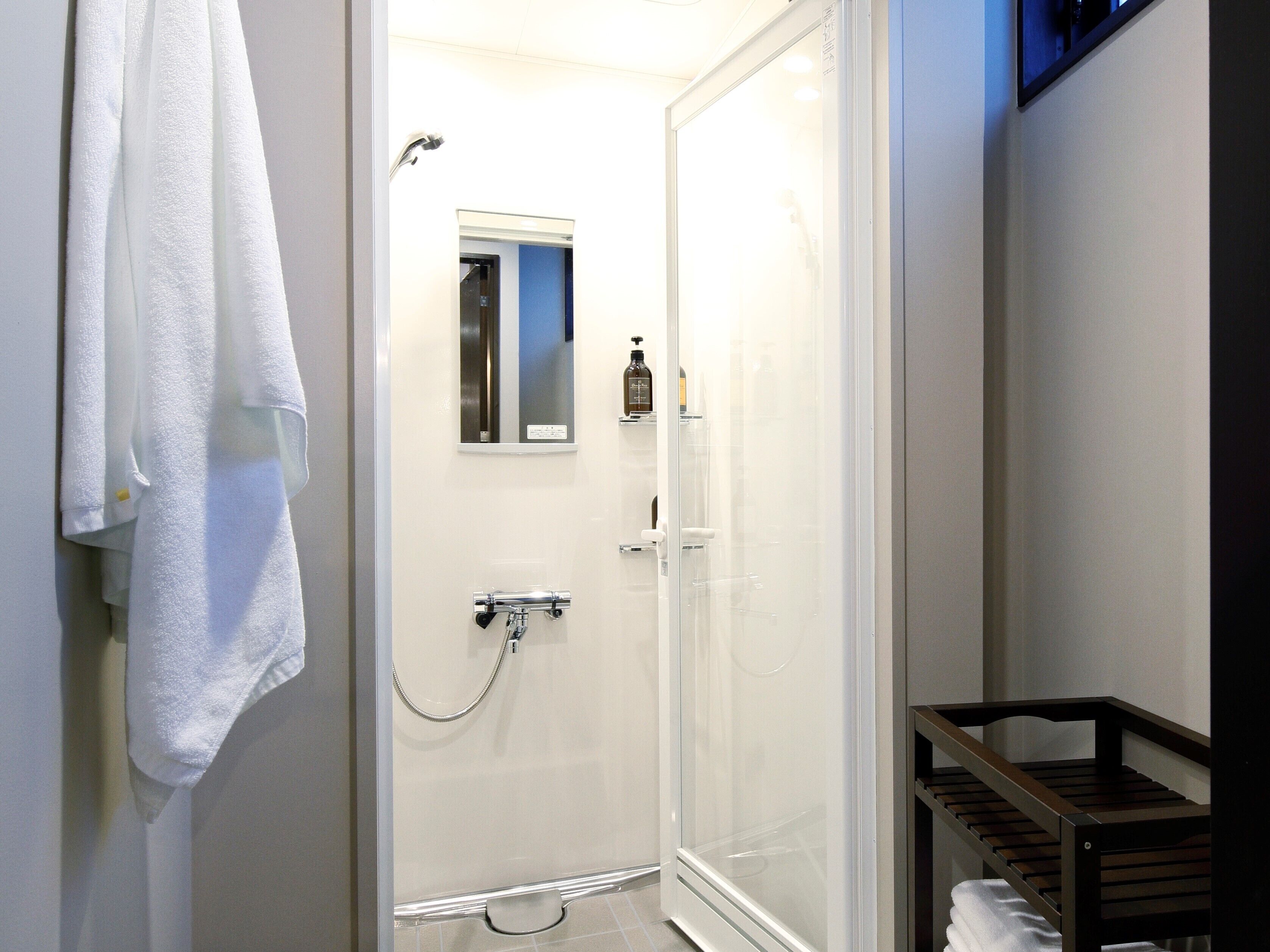 Ein modernes Badezimmer mit einer Duschkabine aus Glas, einem weißen Handtuch an der Wand und einer kleinen Holzablage.