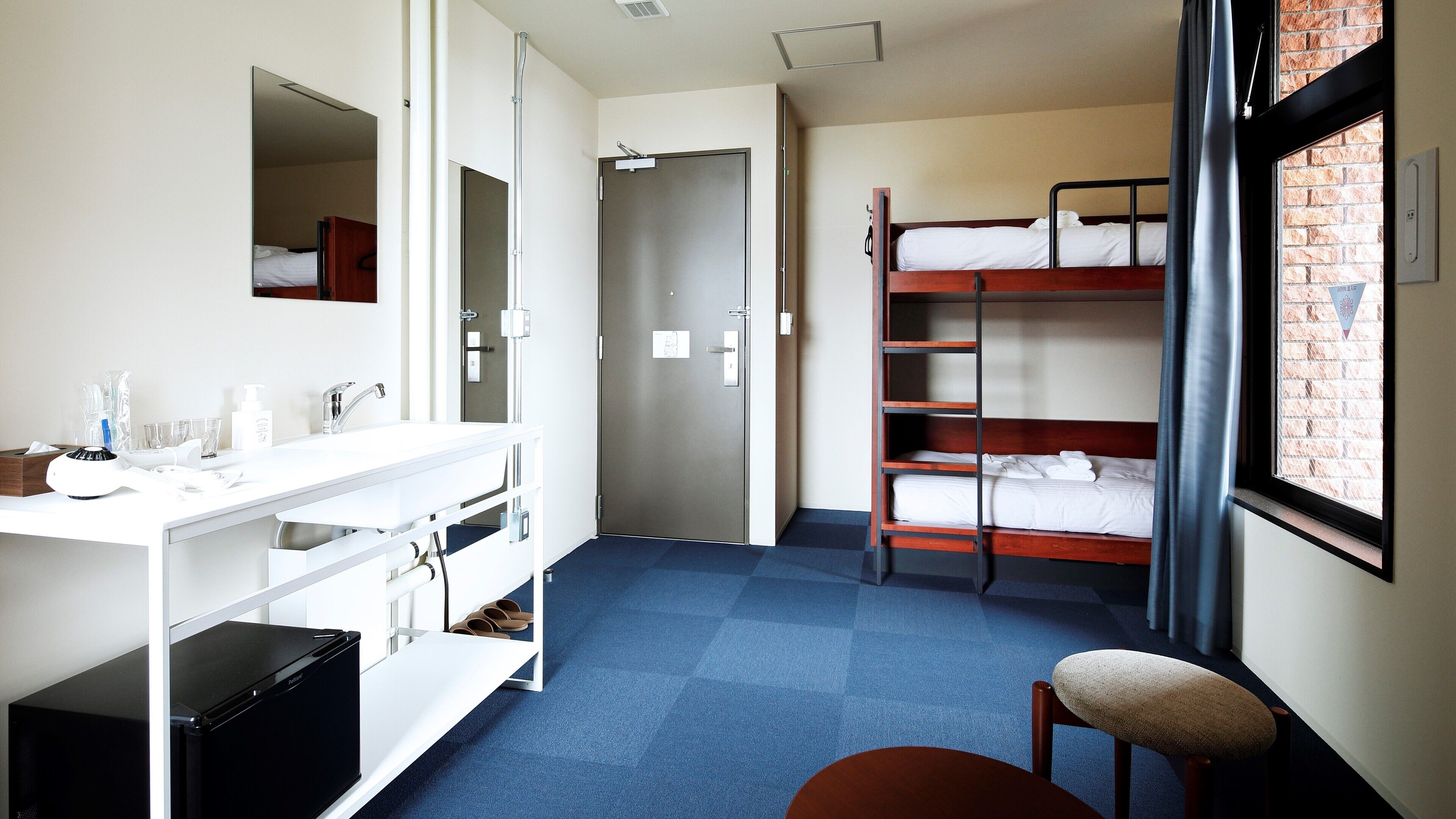 Une chambre d’hôtel avec un lit superposé, un bureau avec un miroir, un lavabo et une chaise.