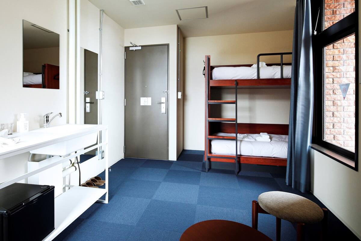 A hotel room with a bunk bed, a desk with a mirror, a sink, and a chair.