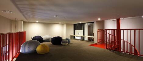 Een modern interieur met vloerbedekking, rode leuningen en diverse grote, kleurrijke poefs.