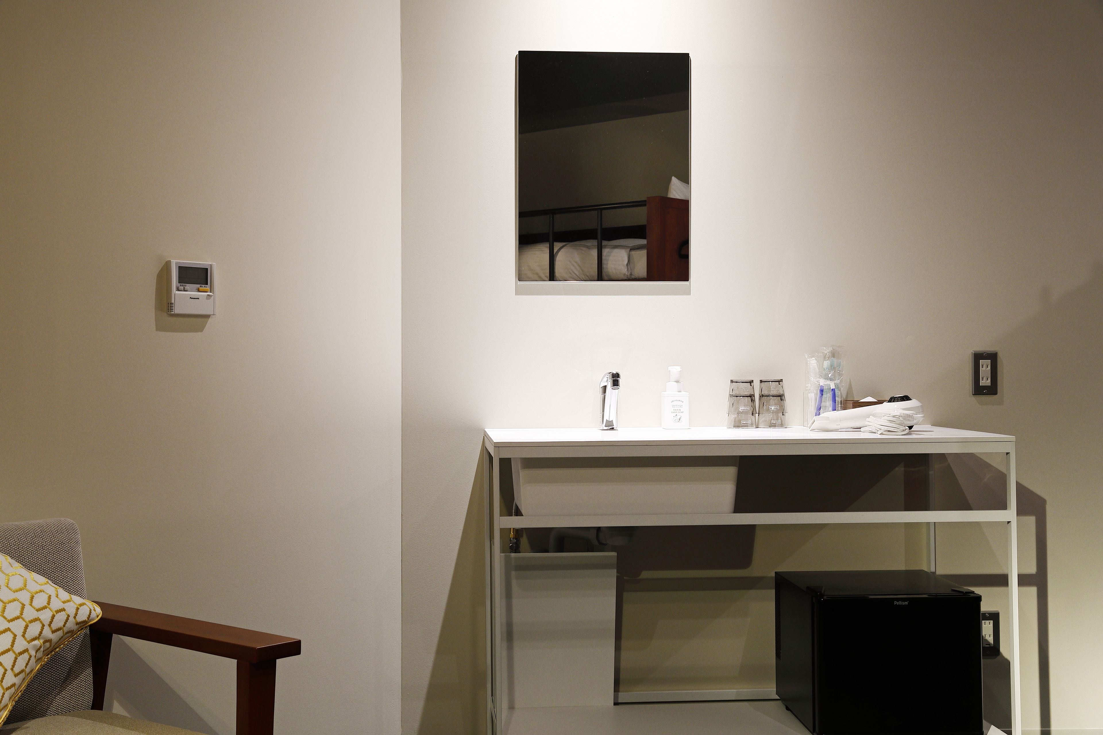 A room with a bed, a small table with toiletries, a wall-mounted heater, and a black speaker.
