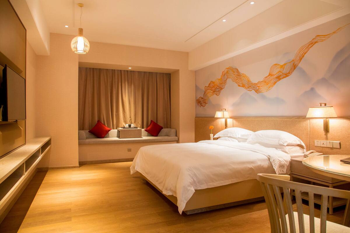 Hotelkamer met een bed, bureau, stoel, televisie, raam met gordijnen en een muurschildering.