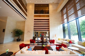 A modern lobby with a high ceiling, a central staircase, and seating areas with red and white furniture. - Kare Prime Hotel Dapeng Shenzhen (Shenzhen)