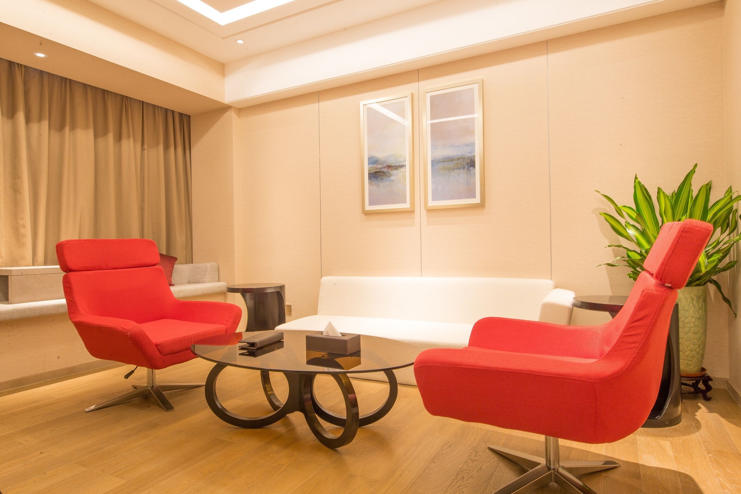Een moderne woonkamer met een witte bank, twee rode fauteuils, een glazen salontafel en een potplant.