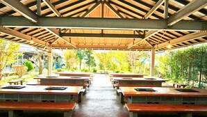 An outdoor covered pavilion with rows of wooden tables and benches, surrounded by greenery. - Oogiyama Ryokan (Fujikawaguchiko)