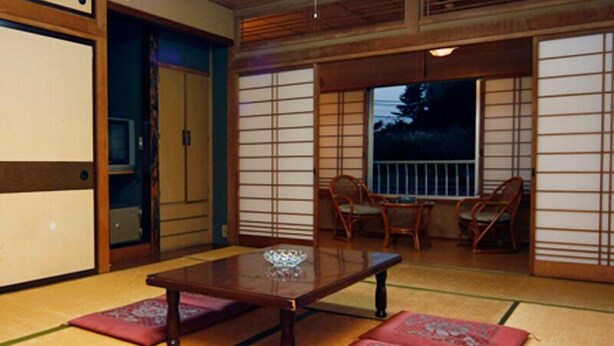 A traditional Japanese room with tatami flooring, a low wooden table, and sliding doors. - Oogiyama Ryokan (Fujikawaguchiko)