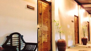 Un pasillo con puertas de madera, un banco y grandes jarrones con plantas.